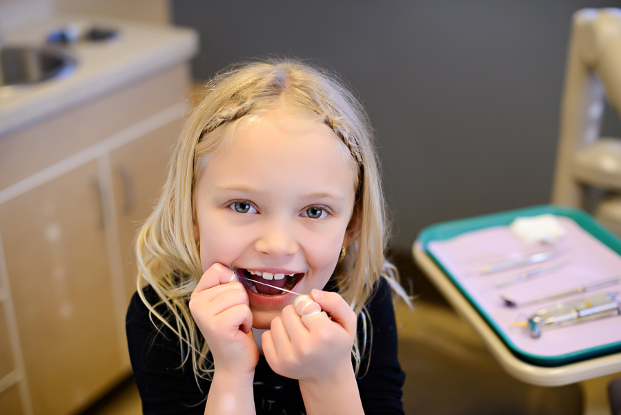 Image of a young patient flossing and waiting to see if she is a candidate for early orthodontic treatment at Woodland Family Dental.